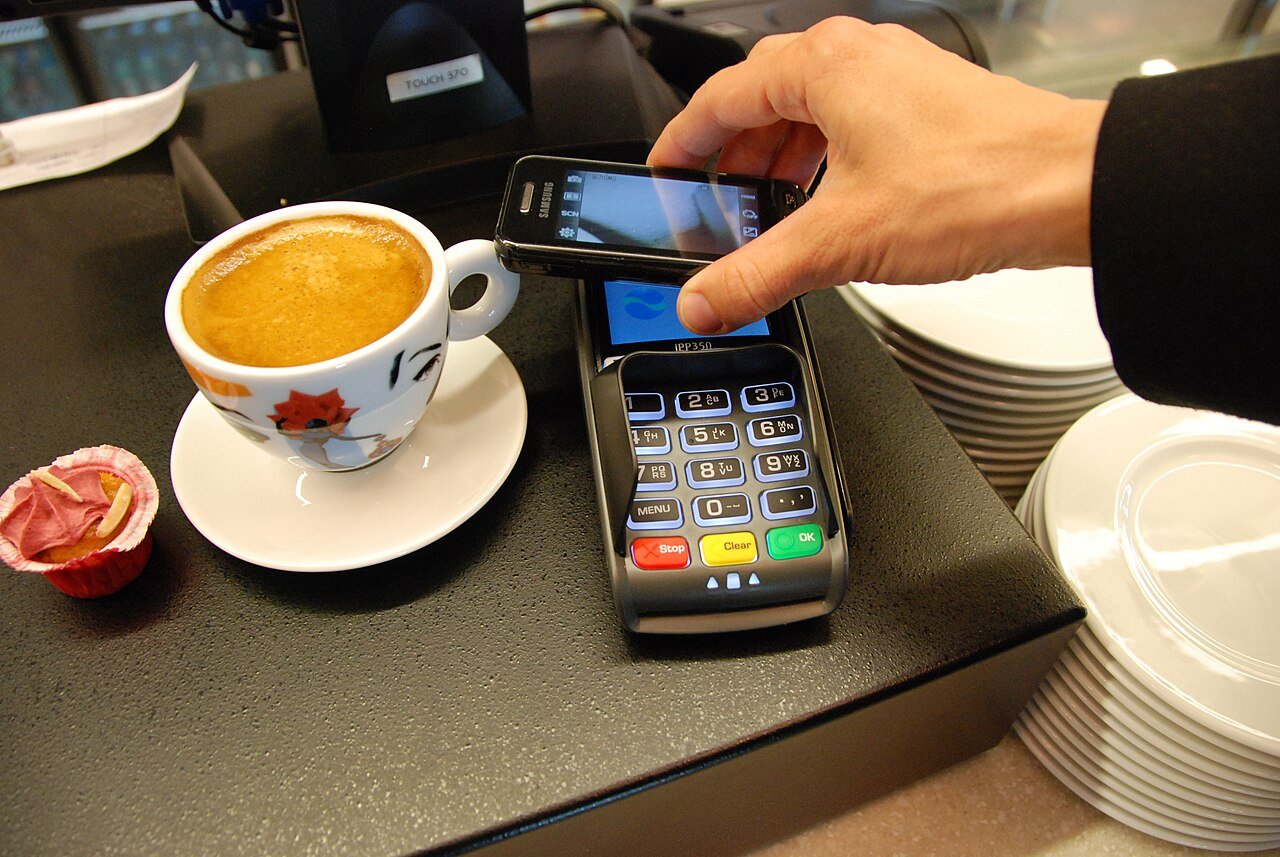A customer uses a mobile phone with a card payment terminal, illustrating tap-to-pay technology
